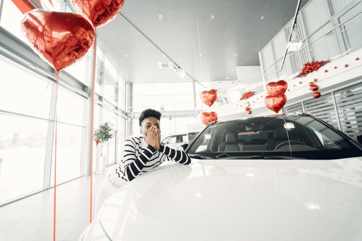 young woman leaning on a new car at car dealership